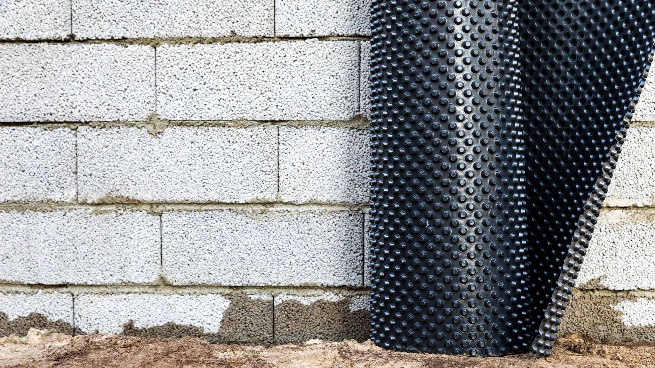 Close-up of black rubber flooring tiles installed against a white brick wall for home renovation.