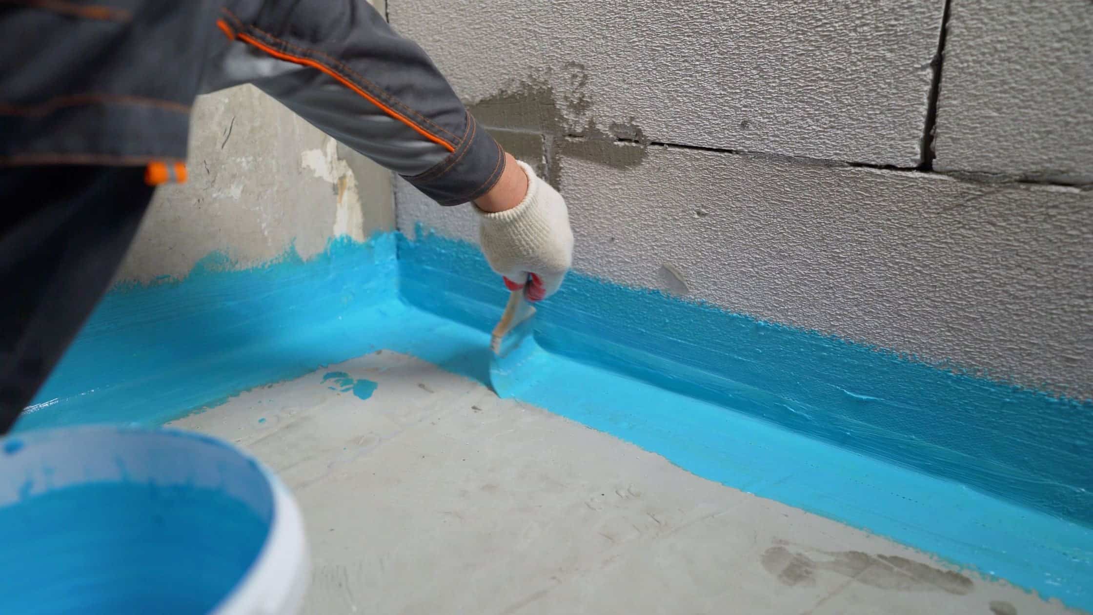Worker applying waterproofing sealant to basement wall for home renovation.