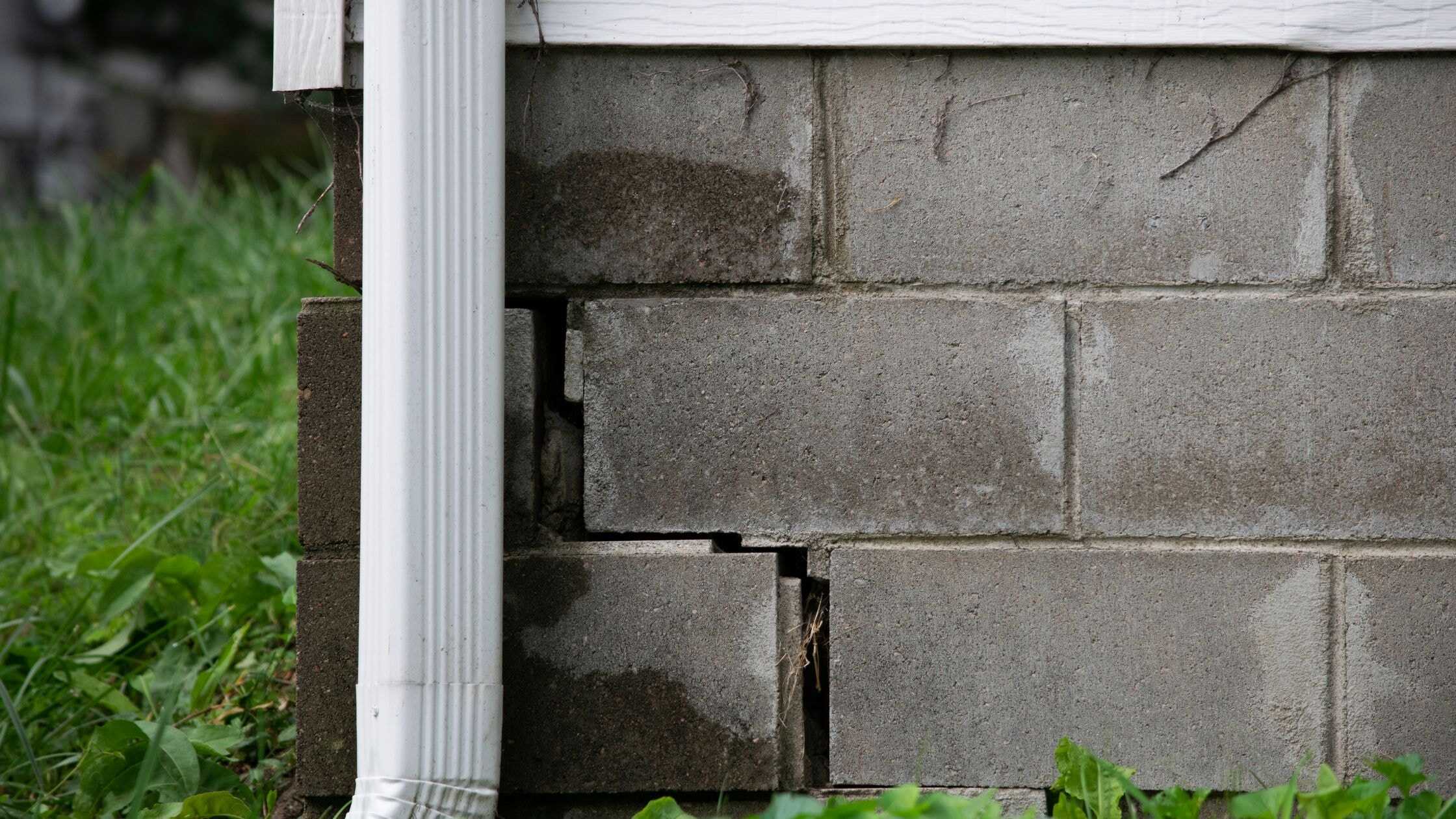 Close-up of damaged brick wall with cracked mortar and missing bricks on a home exterior.