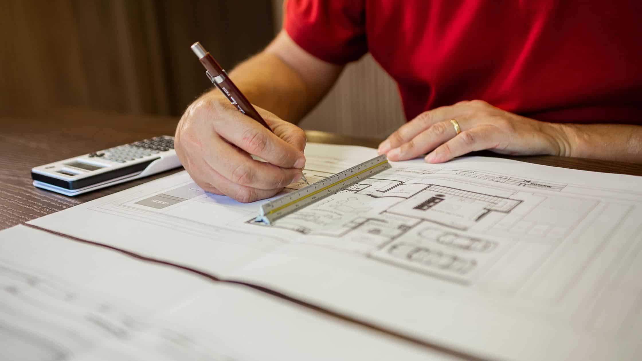 Person drawing home renovation plans with ruler and pencil on blueprint.