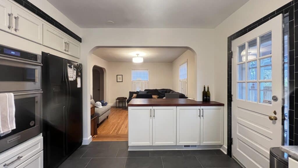 Modern kitchen with black appliances and white cabinets, open to a cozy living room with hardwood fl.