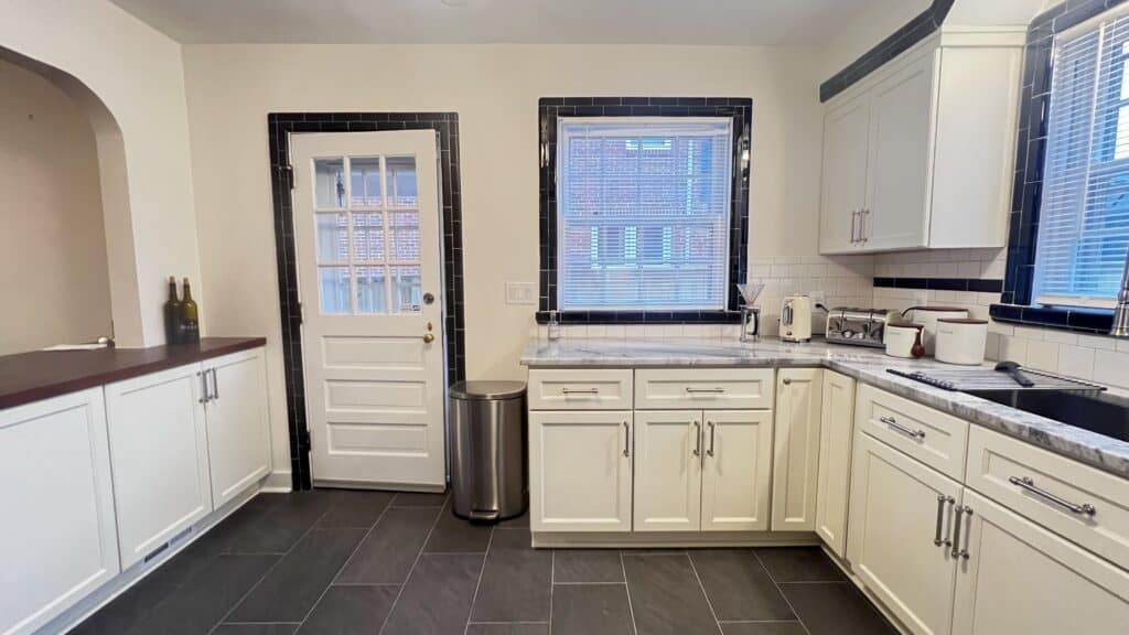 Bright, modern kitchen with white cabinets, black countertops, and large windows.