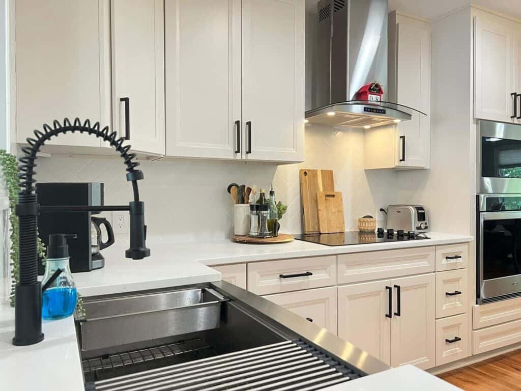 Bright modern kitchen with white cabinets, stainless steel appliances, and black fixtures.