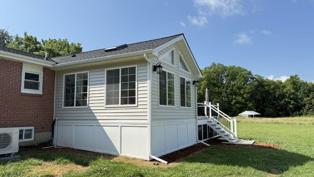 Bright sunroom extension with large windows and white siding, perfect for relaxing and enjoying outd.