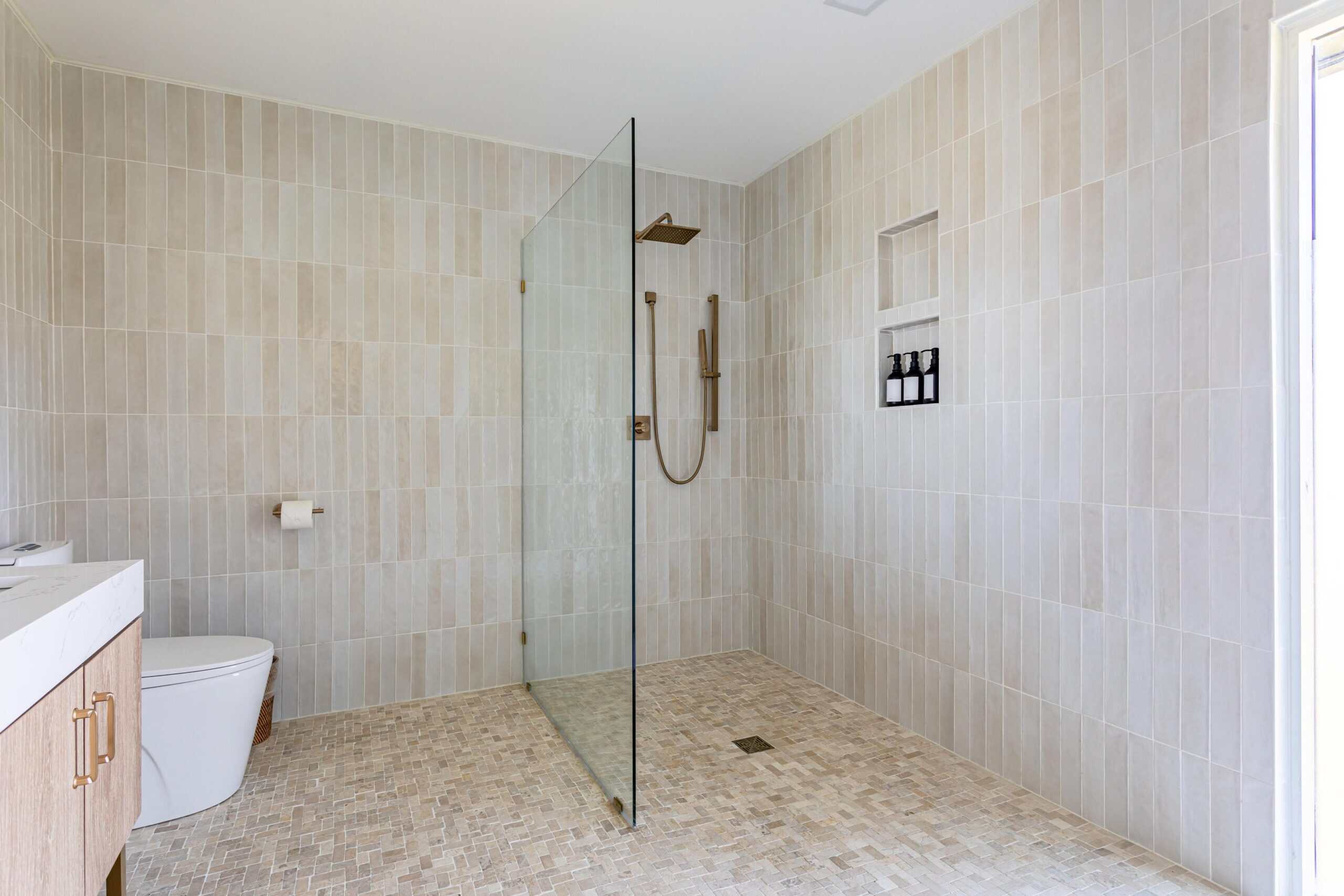 Spacious walk-in shower with glass partition and beige tiles.