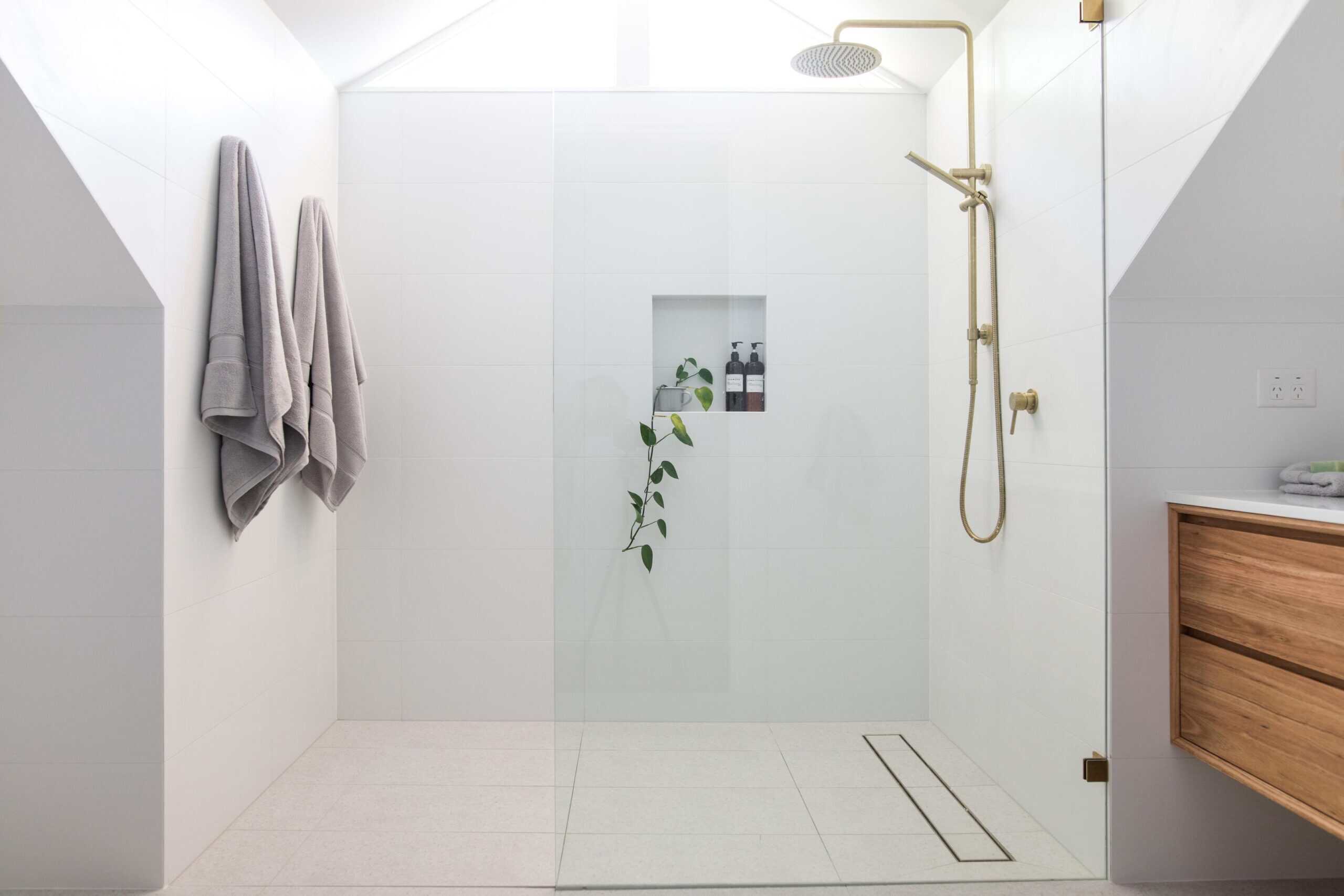 Spacious modern walk-in shower with white tiles and gold fixtures in a bathroom.