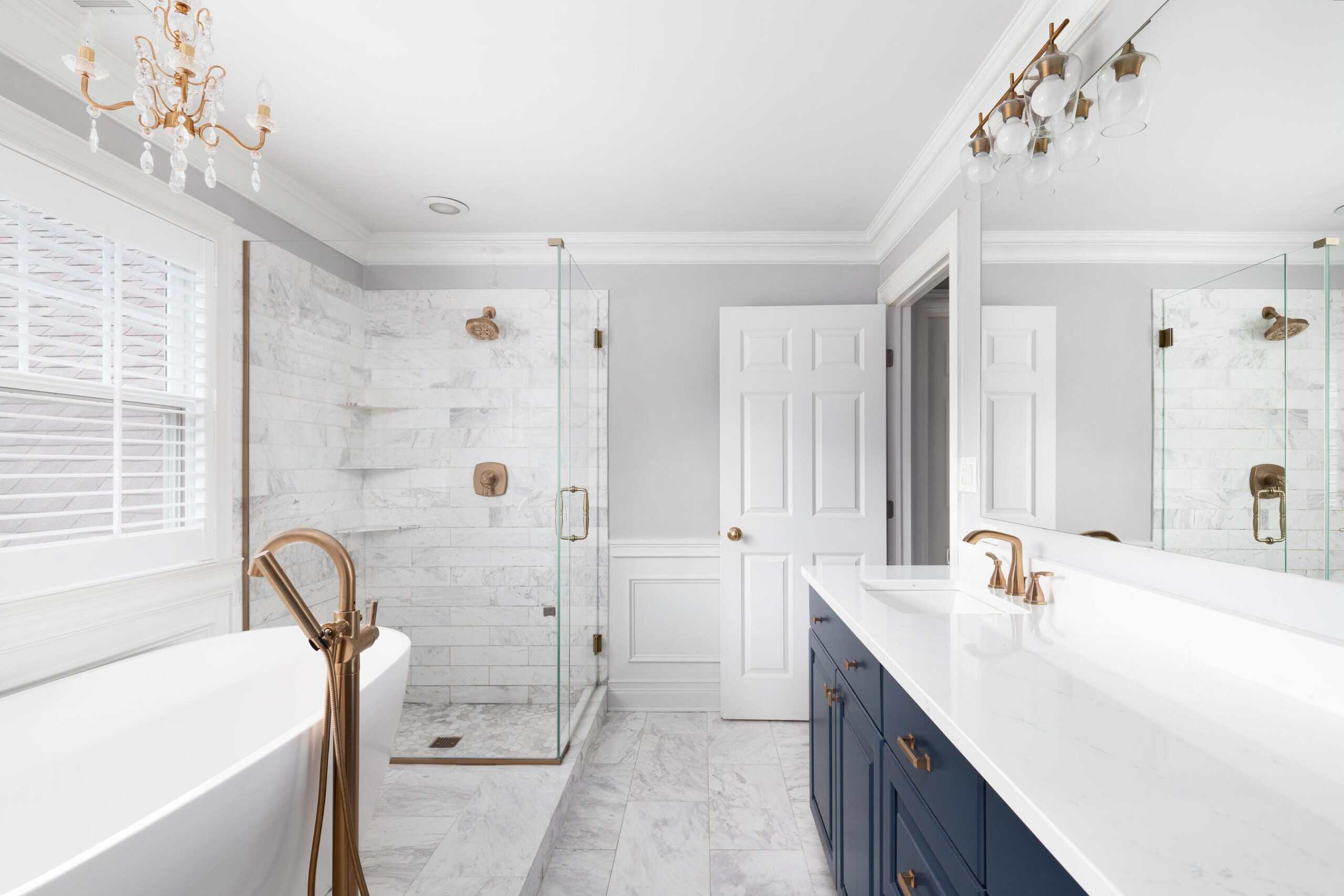 Bright modern bathroom with walk-in shower, bathtub, and navy vanity with gold fixtures.