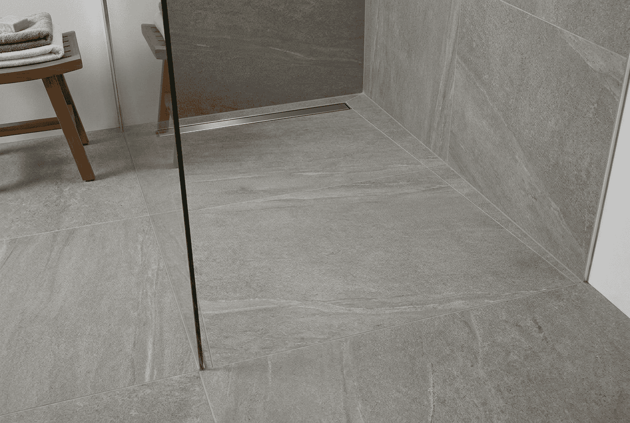Contemporary bathroom shower with large gray tiles and glass partition.